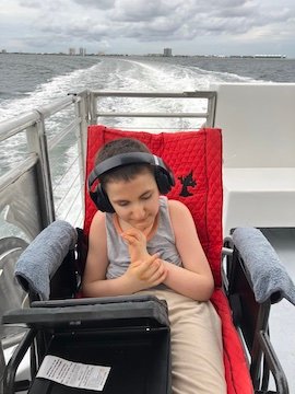 Charlie on a dolphin cruise. Hes wearing his headphines and the water wakes behind him as he sits in his wheelchair.